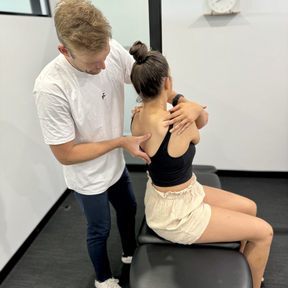 Tim White assessing a seated patient's neck and shoulders